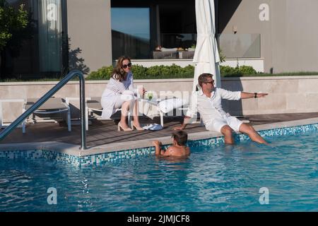 Une famille heureuse profite de vacances dans une maison de luxe avec piscine. Le couple senior passe du temps avec son fils pendant les vacances. Sélection Banque D'Images