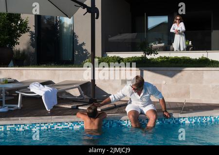 Une famille heureuse profite de vacances dans une maison de luxe avec piscine. Le couple senior passe du temps avec son fils pendant les vacances. Sélection Banque D'Images