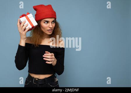 Photo prise d'une belle jeune femme blonde sombre et élégante isolée sur un mur d'arrière-plan bleu portant un petit top noir et un r Banque D'Images