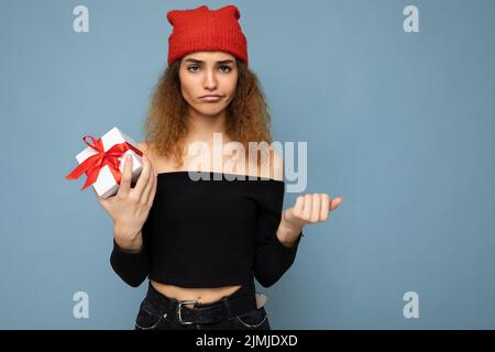 Photo prise de belle insatisfaite jeune blond foncé curly femme isolée sur fond bleu mur portant noir crop top et Banque D'Images