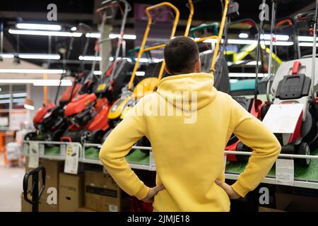 Un client d'un magasin de matériel choisit une tondeuse à gazon électrique ou à gaz Banque D'Images
