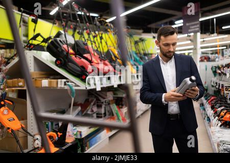Un client d'un magasin choisit de l'huile moteur pour une tondeuse à essence Banque D'Images