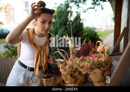 Bonne jeune femme caucasienne choisit des fleurs en pot à acheter à l'extérieur de la cabine de jardin Banque D'Images