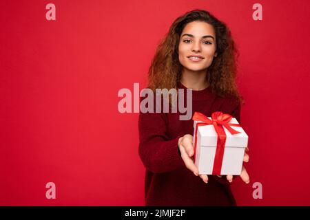 Belle heureuse jeune femme brune isolée sur fond coloré mur portant élégant vêtements décontractés tenant boîte cadeau et Banque D'Images