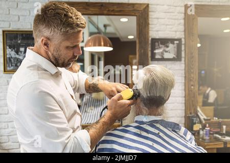 Coiffeur faisant une coupe de cheveux élégante pour un vieil homme beau Banque D'Images