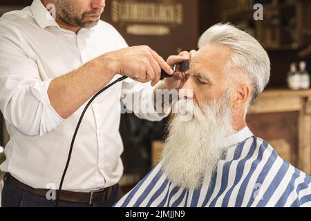 Coiffeur faisant une coupe de cheveux élégante pour un vieil homme beau Banque D'Images