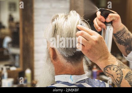 Coiffeur faisant une coupe de cheveux élégante pour un vieil homme beau Banque D'Images