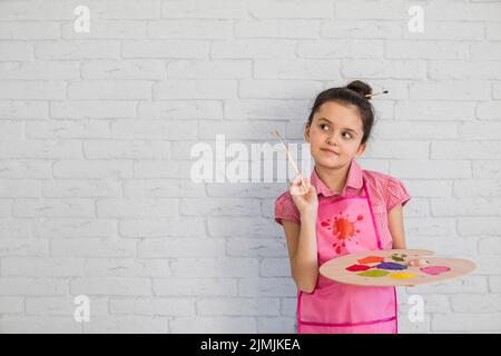 Portrait fille avec palette de pinceaux debout contre le mur blanc Banque D'Images