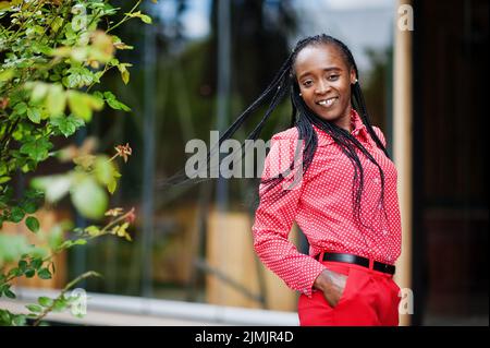 Jolie braides affaires afro-américaine dame brillant bossy personne sympathique porter bureau rouge chemise et pantalon. Banque D'Images