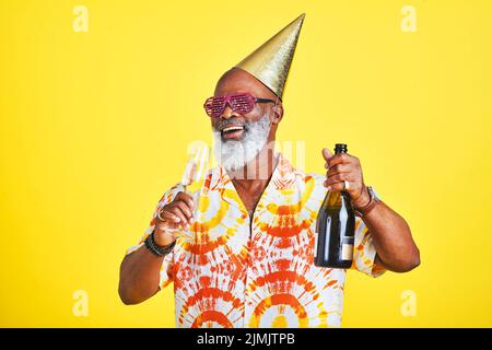 Je suis venu ici pour faire la fête. Un homme de haut niveau drôle et joyeux qui célèbre et boit du champagne en studio sur fond jaune. Banque D'Images