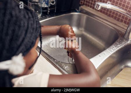 Shes fait toujours ses corvées. Une adorable petite fille faisant les plats dans la cuisine à la maison. Banque D'Images