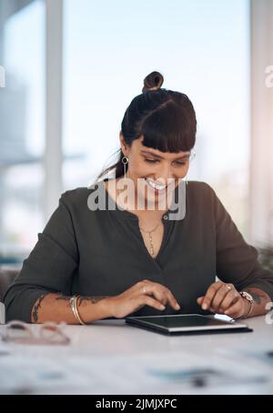 La technologie connecte le monde. Une jeune femme d'affaires attirante assise seule dans son bureau et utilisant une tablette. Banque D'Images