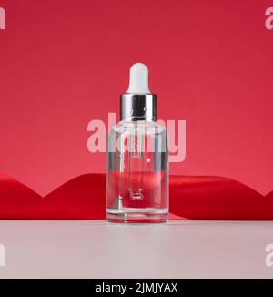 Flacon blanc transparent en verre avec pipette. Contenant pour cosmétiques, acides et huiles sur fond rouge Banque D'Images