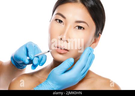 Femme asiatique pendant la procédure d'augmentation des lèvres sur fond blanc Banque D'Images