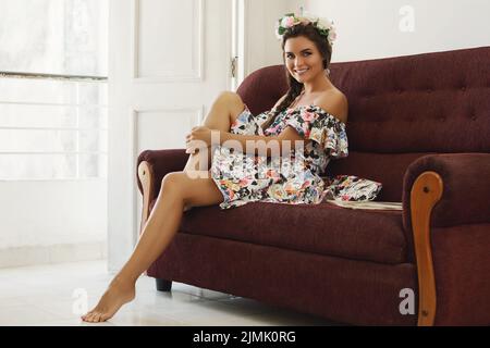 Une femme heureuse dans une belle robe est assise sur le canapé vintage Banque D'Images