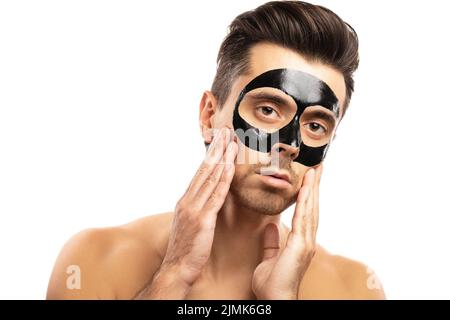 Jeune homme avec un masque noir de charbon de bois sur son visage sur fond blanc. Banque D'Images