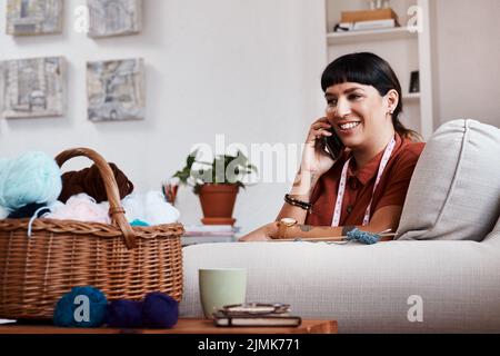Quel pull de couleur voulez-vous. Un designer de vêtements parlant sur son téléphone tout en se relaxant à la maison. Banque D'Images