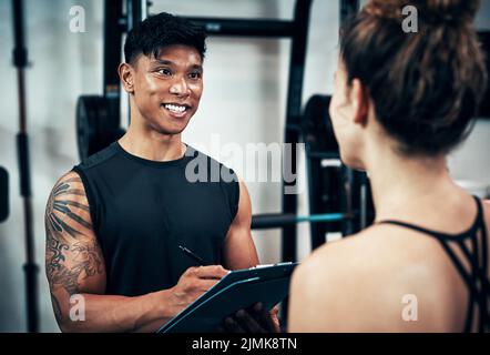 Faisons juste une évaluation rapide du corps. Une jeune femme sportive parlant à un entraîneur de fitness à la salle de gym. Banque D'Images