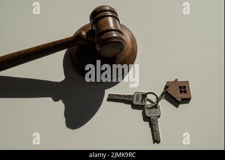 Des clés avec porte-clés en forme de maison et un gavel de juge sur fond blanc. Banque D'Images