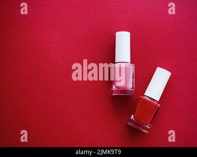 Flacons de vernis à ongles rouges et roses sur fond rouge, manucure et cosmétiques de beauté Banque D'Images