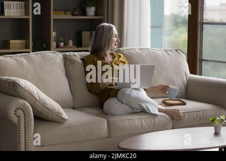 Une femme âgée, souriante et attentionnés, assise sur un canapé à la maison Banque D'Images