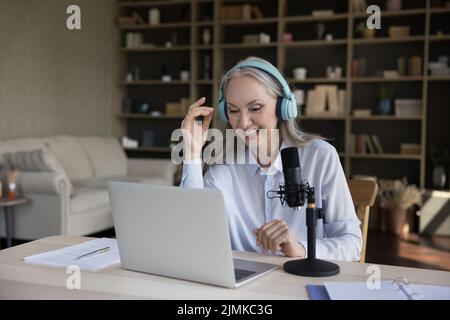 Bonne femme de blogger senior dans le casque parlant au micro professionnel Banque D'Images