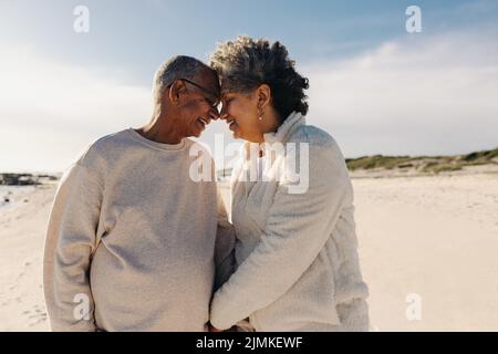 Couple de personnes âgées souriant et se touchant la tête ensemble à la plage. Couple senior joyeux partageant un moment romantique à l'extérieur. Couple heureux Banque D'Images