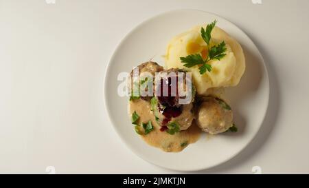 Une assiette de boulettes de viande suédoises avec purée de pommes de terre, sauce crémeuse traditionnelle et baies de lingonis. Banque D'Images