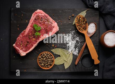 Morceau de viande de bœuf cru, steak de striploin sur fond noir, vue du dessus. Morceau de viande marbré New York Banque D'Images
