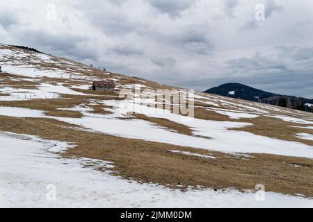 Une prairie alpine enneigée avec une petite cabane. Le ciel est plein de nuages sombres d'orage et témoigne d'une tempête de neige imminente. Banque D'Images