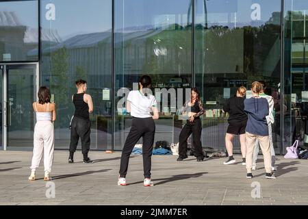 Jeunes adultes ou adolescents pratiquant des mouvements de danse devant la bibliothèque Oodi à Helsinki, en Finlande Banque D'Images