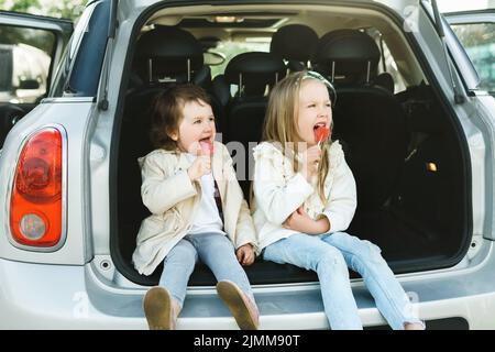 Deux petites filles assises dans le coffre d'une voiture et mangeant des sucettes Banque D'Images