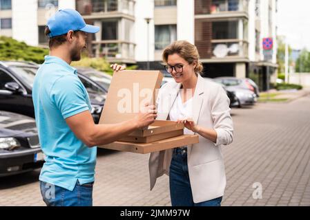 Un livreur portant un uniforme bleu livre une pizza à une femme cliente Banque D'Images