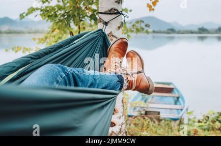 Jeune femme cuir mode bottes photo. Femelle balançant dans un hamac entre les bouleaux sur la rive du lac de montagne. Loisirs en plein air à l'extérieur de la ville Banque D'Images