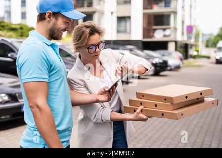 Un livreur portant un uniforme bleu livre une pizza à une femme cliente Banque D'Images