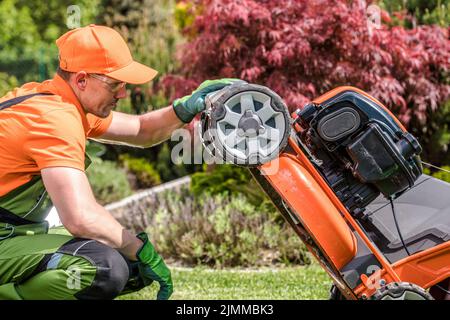 Gros plan sur le jardinier mâle caucasien dans son travail porter soigneusement vérifier son robot de tonte professionnel avant de couper l'herbe. Gar Banque D'Images