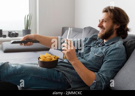 Homme de taille moyenne avec boisson regardant la télévision Banque D'Images