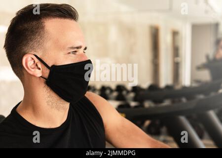 Jeune homme sportif portant un masque de prévention pendant son entraînement en salle de gym Banque D'Images