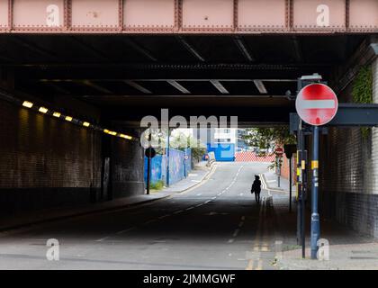 Une femelle seule marchant sous le pont sur une rue déserte dans le quartier délabré du centre-ville. Des rues et des routes vides femme sur son propre silhouetted. Banque D'Images