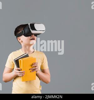 Garçon utilisant un casque de réalité virtuelle tout en tenant des livres Banque D'Images