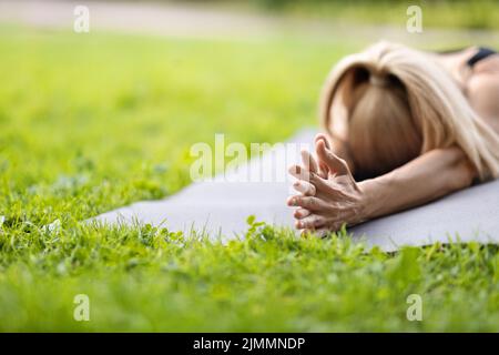 Gros plan d'une dame blonde non reconnaissable, allongé sur un tapis de yoga Banque D'Images