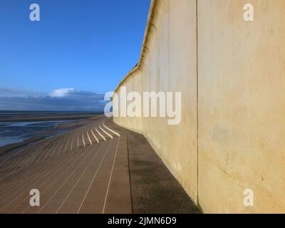 Vue en perspective sur le sentier côtier en béton de blackpool avec des marches menant à la plage dans la lumière chaude de l'après-midi avec du bleu Banque D'Images