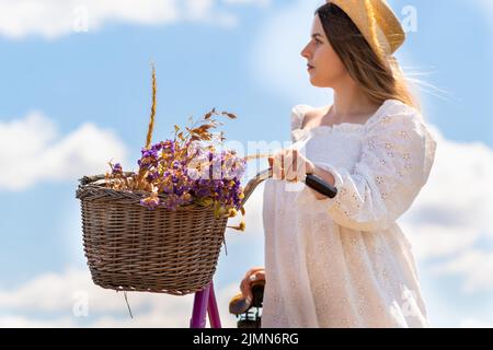 Portrait court d'une jeune femme avec des fleurs de lavande dans le panier de sa bicyclette contre un ciel bleu Banque D'Images