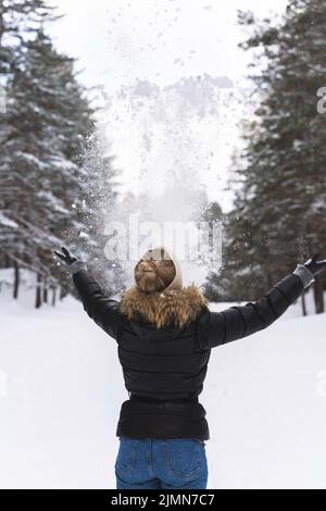 Femme jetant de la neige dans l'air pendant la journée froide d'hiver Banque D'Images