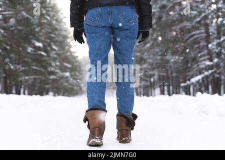 Femme portant des bottes en peau de mouton marchant sur une route enneigée Banque D'Images