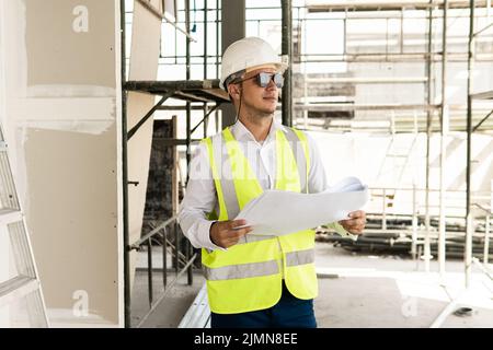 Homme architecte portant un gilet de sécurité avec des plans sur un chantier de construction Banque D'Images