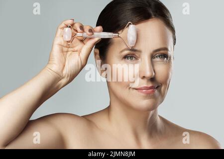 Belle femme d'âge moyen utilisant un rouleau de quartz rose Banque D'Images