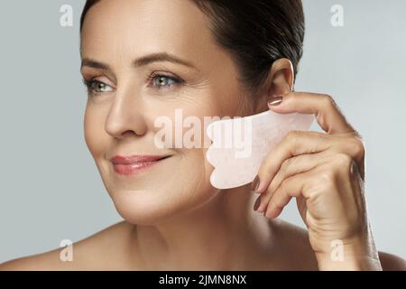 Belle femme d'âge moyen faisant un massage facial avec une rose Gua Sha pierre Banque D'Images