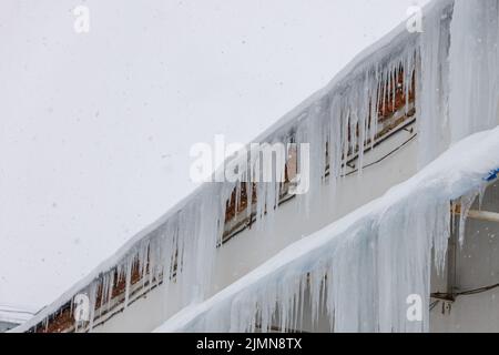 rangée de glaçons accrochée sur les bords du toit le jour d'hiver pendant la neige Banque D'Images