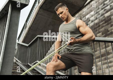 Homme musclé pendant l'entraînement avec un élastique de résistance sur une rue Banque D'Images